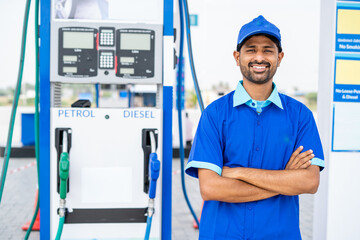 Happy petrol pump worker standing with crossed arms by looking camera at gas filling station - concept of successful, employment and petroleum service.