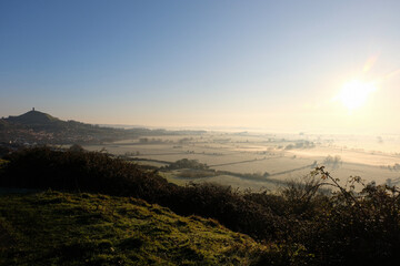 The historic landmark of St Michael's Glastonbury Tor tower overlooking the beautiful rural countryside of Somerset levels with stunning early morning light mist and fog © Travelanza
