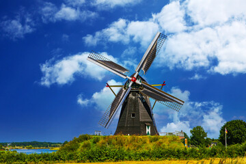 Beesel, Netherlands - Juin 9. 2021: View on one typical wooden dutch windmill (Molen de grauwe beer) in rural landscape against  blue summer sky with fluffyclouds, river maas background
