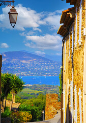 View beyond ancient mediterranean natural stone house wall, street lamp from hill top village...