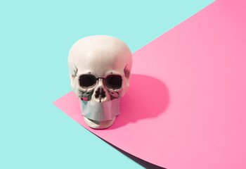 Skull with duct tape across the mouth on a pink and blue background. Silence, propaganda concept.