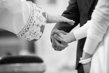 foto in bianco e nero della mano di un prete che da la benedizione a degli sposi 