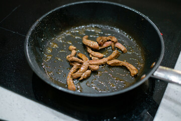 Frying meat in a frying pan on an induction cooker.