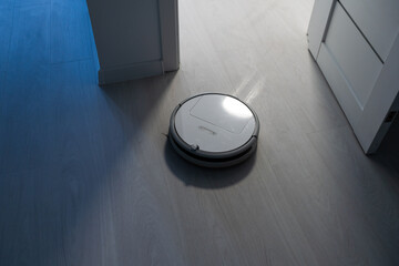 Robotic vacuum cleaner on laminate wood floor in bedroom.