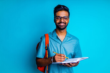 handsome young bearbed indian man with eye glasses in blue cotton t-shirt with orange rainbow backpack in studio background