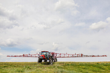 Farmer in tractor at industrial crop farm field spraying green wheat field with herbicides...