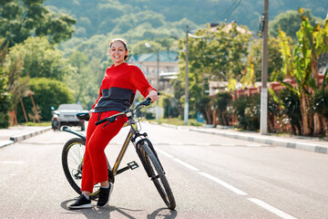 Sports lifestyle. Full-length portrait of a Young smiling woman in sportswear, leaning on a Bicycle. In the background, an empty road and street. Eco-friendly transport concept