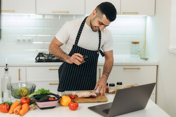 Smiling guy prepares vegetables in the kitchen. Dressed in a black apron