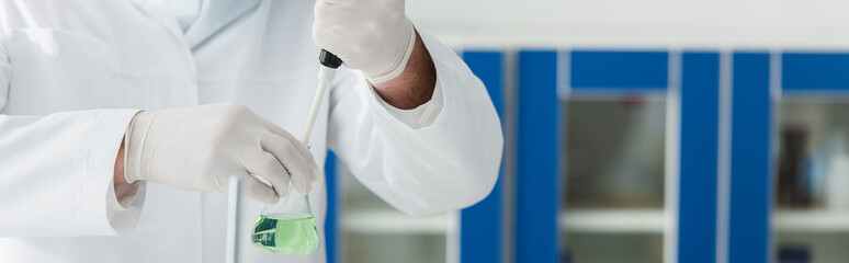 partial view of biologist holding micropipette and flask with liquid, banner.
