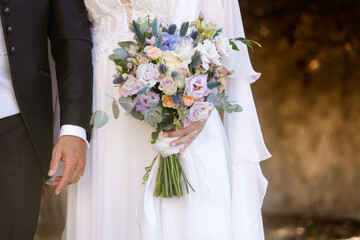 dettaglio di un bouquet di fiori tenuto in mano da una sposa con accanto il suo sposo 