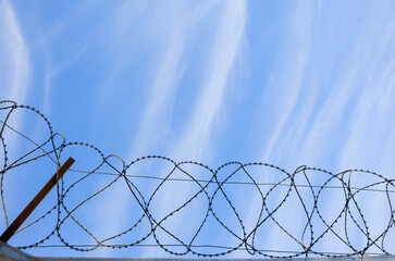 Fence with barbed wire is under blue sky, border background, close-up
