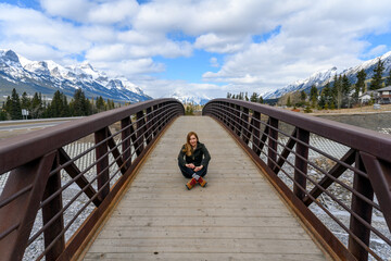A middle aged woman sitting in the middle of a wood pedestrian bridge over Cougar Creek