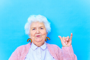 mature woman with snow white grey white hair in pink cardigan and blue shirt wear rainbow colorful earrings in studio background