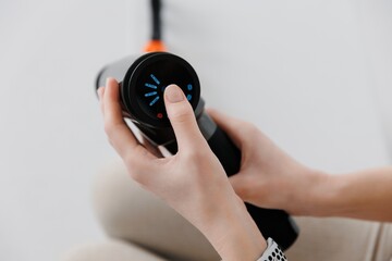 Girl holding a therapeutic percussive vibrating massage gun in her hand. Adjusting the device. Sports recovery concept after a workout. 