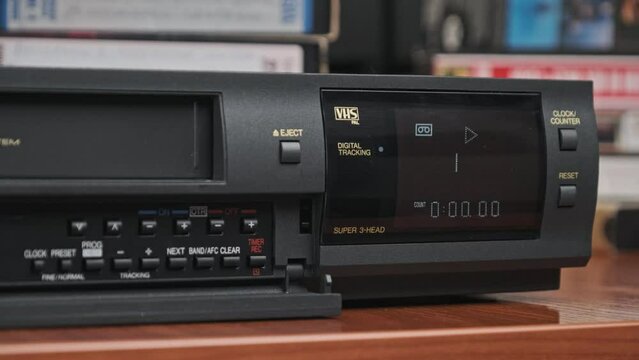 Insert VHS cassette into VCR and push play button. Black vintage videotape cassette recorder with counter on desk with many video cassettes. Inserting old VHS Tape into retro player. Home video archiv