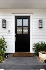 Black front door with windows that have a design element to them with two light fixtures and...