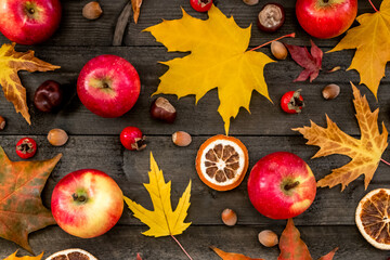 Autumn background maple leaves, apples, rose hips, nuts, chestnuts, dried oranges on a wooden table
