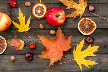 Autumn background maple leaves, apples, rose hips, nuts, chestnuts, dried oranges on a wooden table
