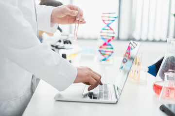 cropped view of geneticist with test tube using laptop in laboratory.