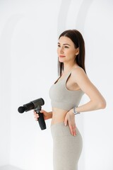 The girl has her hand on her lower back. sore back. the therapeutic percussion vibrating massage gun in her hand. Sports recovery concept after a workout.   