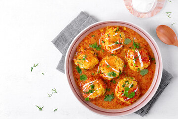 Malai Kofta served with yogurt and fresh herbs. Hot meal with potato and paneer cheese balls in tomato sauce. Indian cuisine. Top view