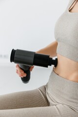 Athletic young woman massaging abs with hand massage gun, post-workout recovery. Physical therapy. 