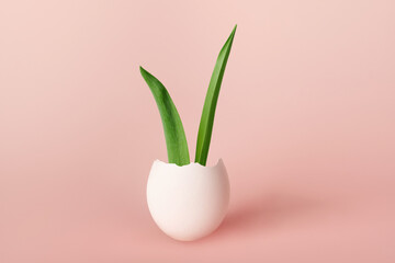 Happy Easter creative concept. Bunny rabbit Ears from green leaves in an Easter egg on pink background