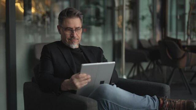 Businessman using tablet computer in office. Happy middle aged man in business casual, Entrepreneur working online, reading finance report, thinking.