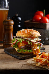 Burger classique fait maison sur une planche rustique avec des frites et une bière. 