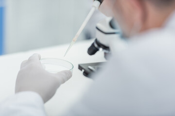 partial view of scientist with micropipette and petri dish in bio laboratory.