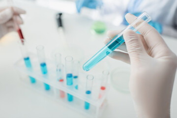 cropped view of scientist holding test tube with blue liquid on blurred background.