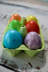 colorful easter eggs in a egg carton box on wooden kitchen table close up
