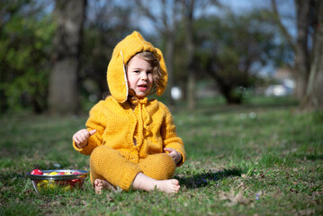 Little girl in a rabbit costume is sitting in the park with colorful eggs on Easter day