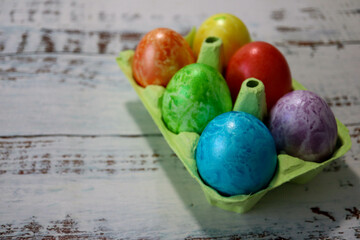 colorful easter eggs in a egg carton box on wooden kitchen table close up