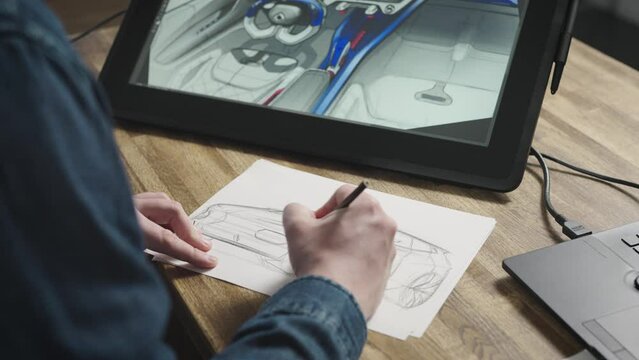 Close up of hands drawing with pencil on paper. The designer sketches a new car on a piece of paper. Modern design studio with equipment.