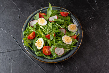 Salad with cherry tomatoes, fresh arugula and quail egg. Concept for a tasty and healthy meal. Vitamins in vegetables and herbs for immunity against the virus. Top view. Copy space