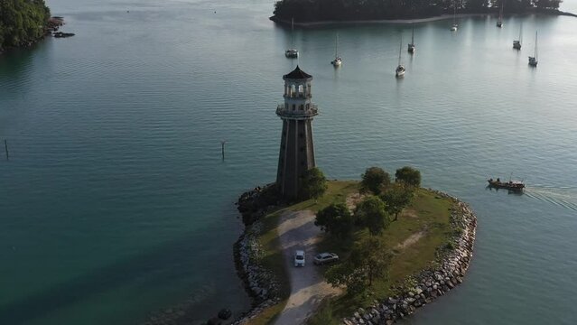 Slow pan shot around beautiful promontory with perdana quay light house in the center, local fishing boat cruising towards telaga harbor marina at langkawi island, kedah, archipelago of malaysia.