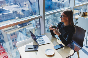 Happy european woman working online in cafeteria using laptop and coffee copy space. Successful female freelancer typing on laptop, remote work