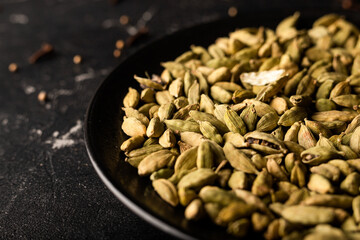 seeds on spoon. Cardamom on the black plate on the black background 