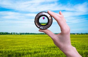 Hand holds optic lens and looking nature with hot air balloon