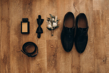 Wedding rings, perfume, shoes and belt. Male attributes on a wooden floor. selective focus