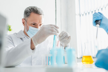 bioengineer in medical mask holding test tubes in laboratory.