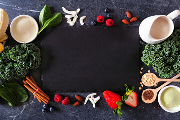 Healthy food frame with blank slate board. Smoothie making concept. Overhead view on a dark stone background. Copy space. Fruit, yogurt, almond milk and a selection of ingredients.
