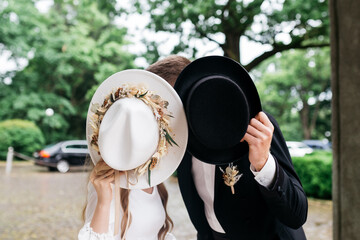 The bride and groom hold hats in their hands. The bride and groom at the wedding.