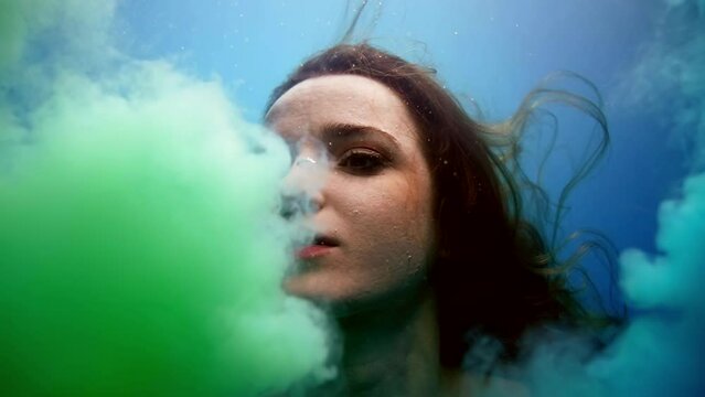 young lady is floating in pool, clouds of green and blue paints are covering her face and hair