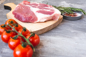 fresh meat steak on a wooden board with rosemary, spices and cherry tomatoes. On a concrete background.