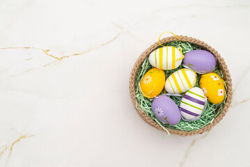 colorful Easter eggs in a knitted basket on a marble background. copy space.