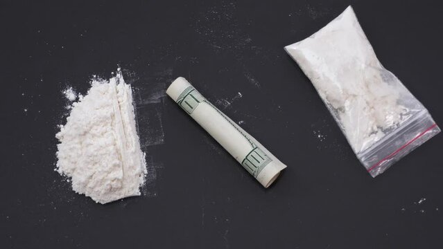 A white substance in a transparent bag, a dollar bill rolled into a tube removes tracks of powder on a black table. The concept of drug addiction, drug use, illegal action. Stop motion animation.