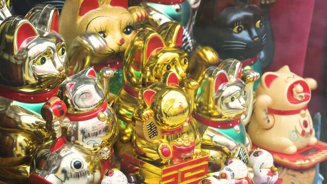 Multiple traditional Japanese maneki neko beckoning cat moving paw figurines on a store display, group of objects, tourist souvenirs sold at the store, products on display, good luck charm concept