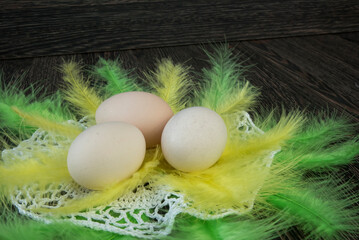 trzy jajka, pisanki, ułożone na żółto zielonych piórach na serwecie robionej na szydełku